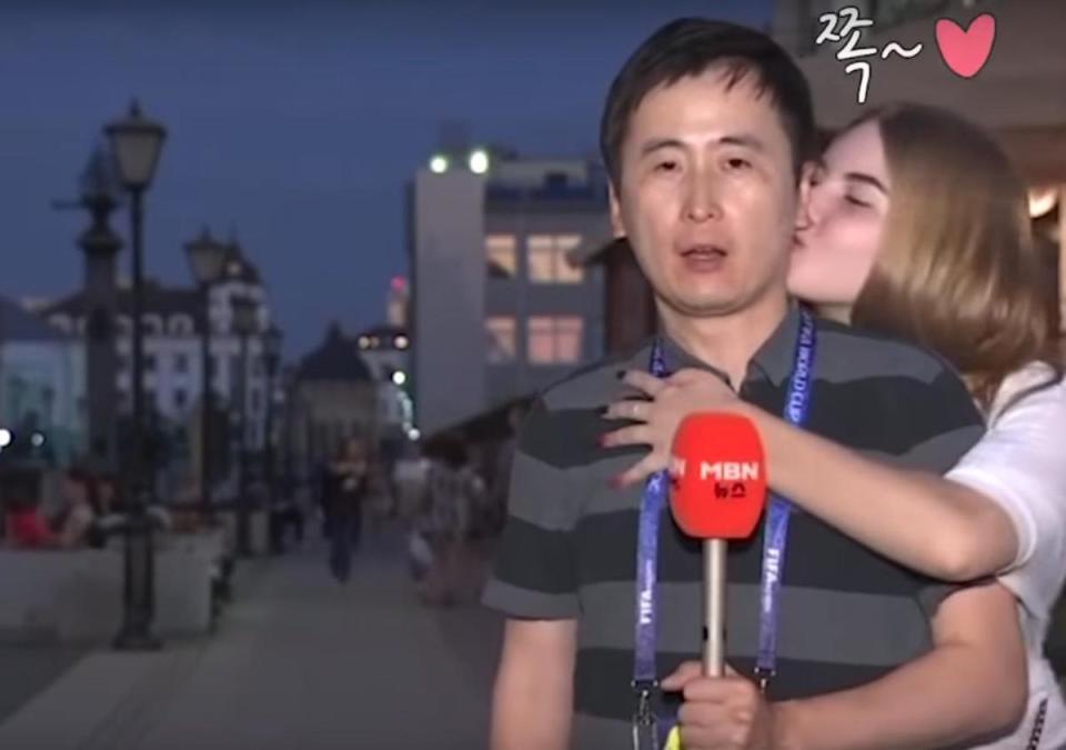 男記者與棚內進行連線中，突然遭2名俄羅斯女子接連狂吻，他假裝淡定持續報導。（翻攝自YouTube）
