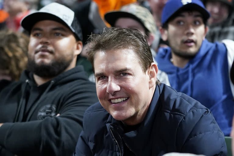 El actor Tom Cruise sonríe durante un juego de béisbol que disfrutó junto a su hijo Connor, que aparece a su lado con un buzo negro y una gorra