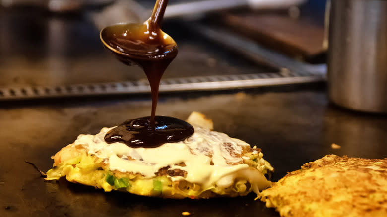 Sauce being ladled onto okonomiyaki