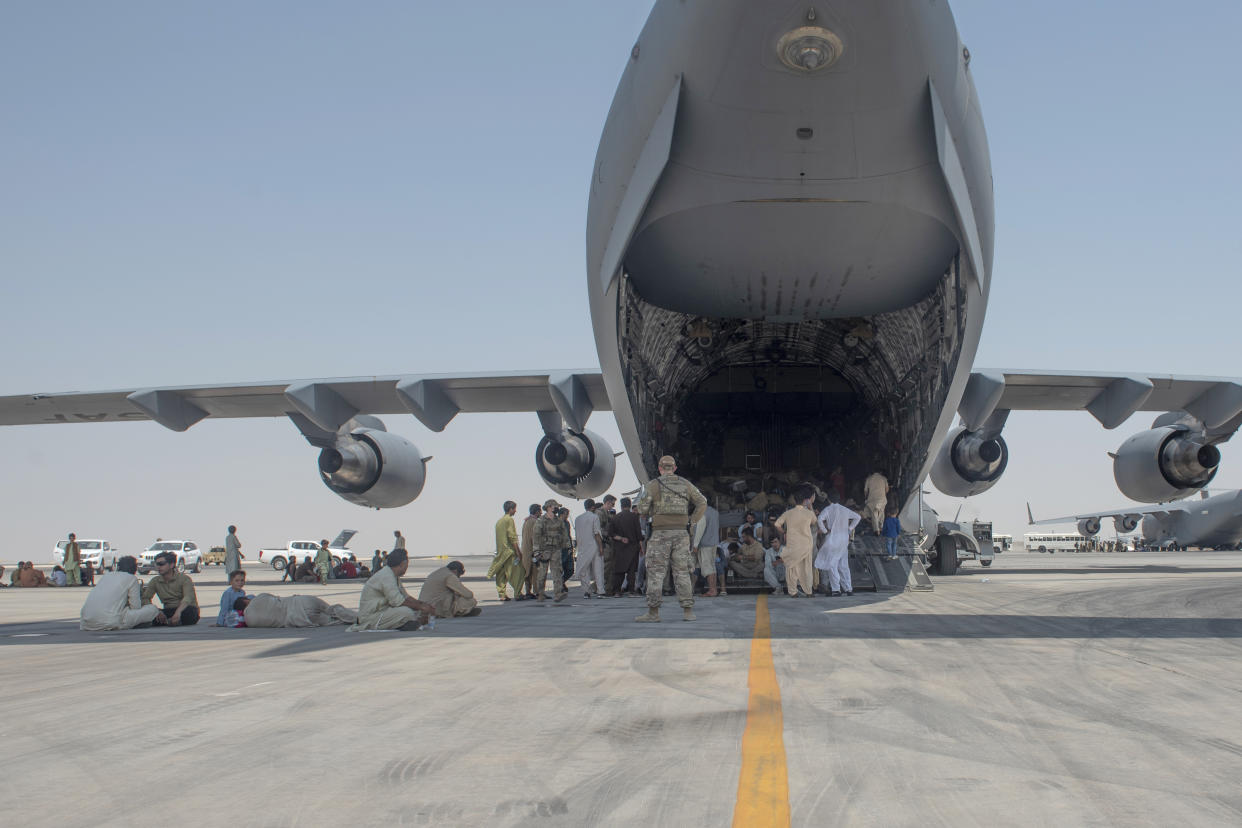 In this photo provided by the U.S. Air Force, evacuees wait under the wing of C-17 Globemaster lll after arriving in an undisclosed location in the Middle East region on Friday, Aug. 20, 2021, after being evacuated onboard a military aircraft from Hamid Karzai International Airport in Kabul, Afghanistan, as part of Operation Allies Refuge. (Airman 1st Class Kylie Barrow, U.S. Air Force via AP)