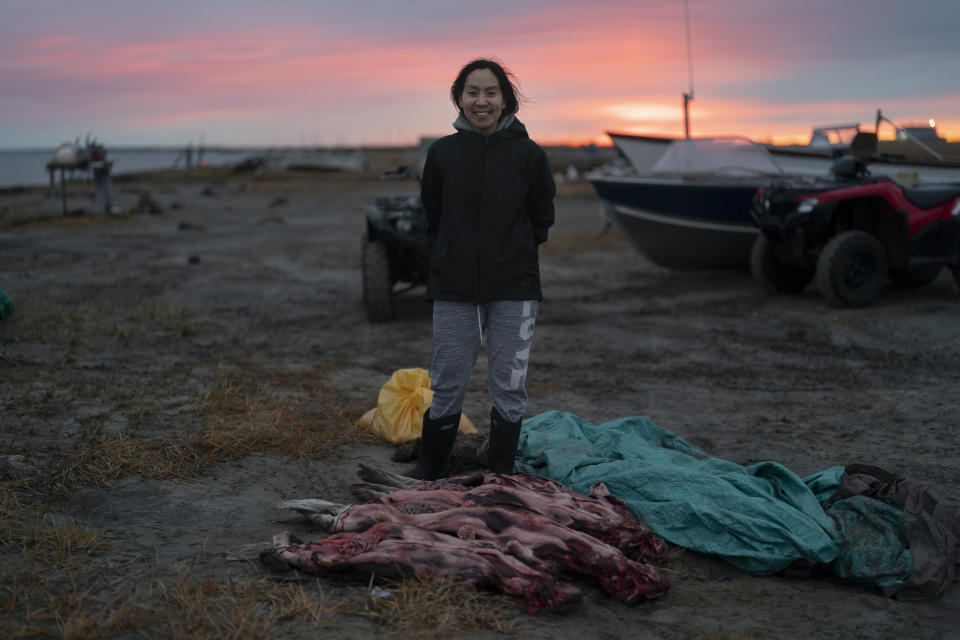 The setting sun colors the sky as Helen Kakoona, 28, stands for a photo with skinned seals in front of her in Shishmaref, Alaska, Monday, Oct. 3, 2022. "Home sweet home," Kakoona said of the village. "No other place feels like home but here." (AP Photo/Jae C. Hong)