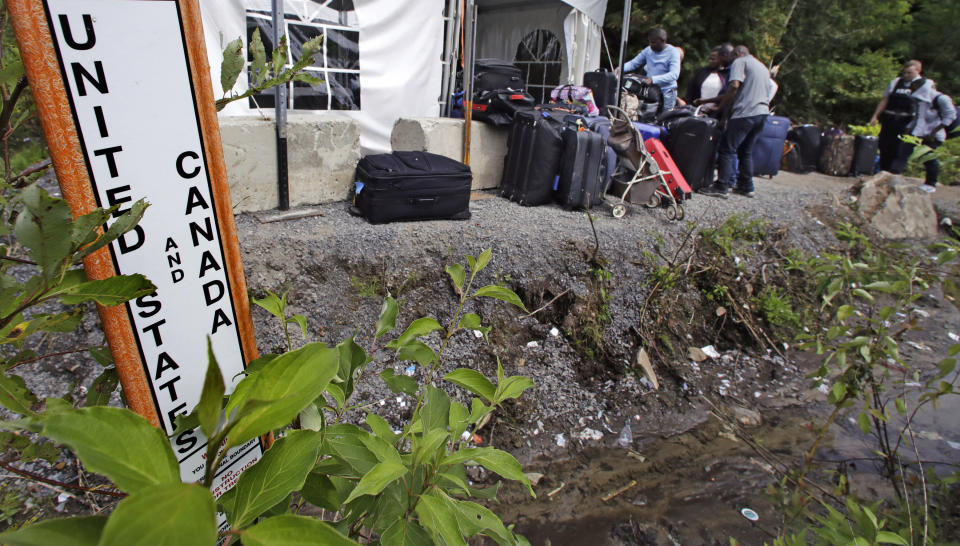 FILE- In this Aug. 7, 2017, file photograph, migrants stack their luggage outside a makeshift police station after crossing illegally into Canada at the end of Roxham Road in Champlain, N.Y., while heading to an unofficial border station across from Saint-Bernard-de-Lacolle, Quebec. Since early 2017, when people who despaired of finding a permanent safe haven in the United States began turning to Canada for help, around 50,000 people have illegally entered Canada, many through Roxham Road in upstate New York. A case being heard in a Toronto court could end the use of Roxham Road. (AP Photo/Charles Krupa)