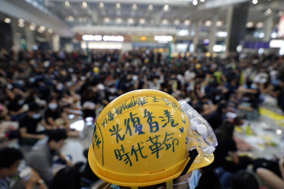 A protester wears a helmet which reads: "Recover Hong Kong, an era's revolution" during a demonstration at the airport in Hong Kong Friday, Aug. 9, 2019. Pro-democracy activists rallied at Hong Kong's airport Friday even as the city sought to reassure visitors of their welcome despite the increasing levels of violence surrounding the 2-month-old protest movement. (AP Photo/Vincent Thian)