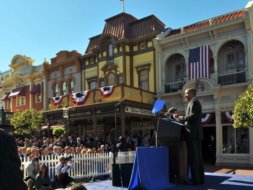 Obama standing at a podium overlooking a crowd and old fashioned building and store fronts.