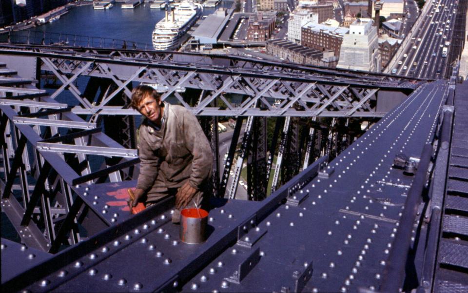 Paul Hogan sitzt auf einer Autobahnbrücke und malert