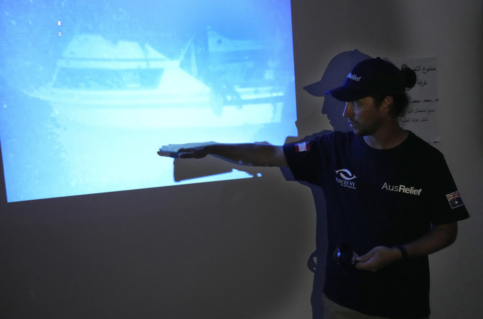 Captain Scott Waters, who drove the small, 3-person underwater craft, a Pisces VI submarine, explains to journalists on a light projector that shows the sank boat during a press conference at the Lebanese navy base, in Tripoli, north Lebanon, Friday, Aug. 26, 2022. The Lebanese navy and a submarine crew announced that they found the remains of at least seven of the approximately 30 drowned migrants in a sunken ship off the coast of Tripoli. (AP Photo/Hussein Malla)