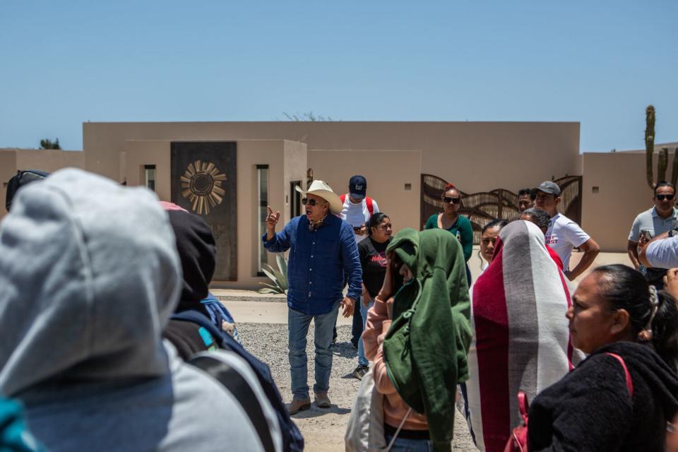 A man in a western-style hat speaks to people in a sunny courtyard