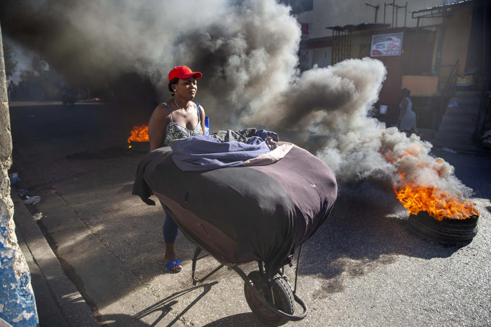 A woman pushes her merchandise away from tires set fire by protesters during a countrywide strike demanding the resignation of Haitian President Jovenel Moise in Port-au-Prince, Haiti, Monday, Feb. 1, 2021. Opposition leaders are pushing for Moïse to step down on Feb. 7 while Moïse has said his term ends in February 2022. (AP Photo/Dieu Nalio Chery)