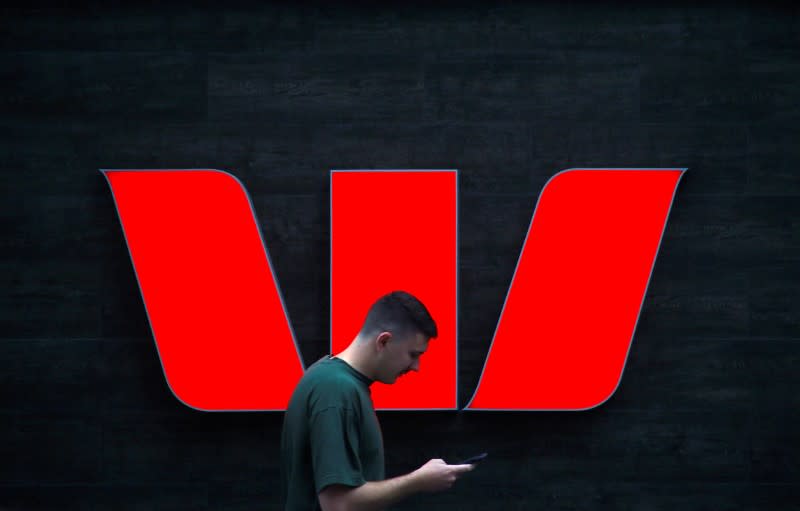 A pedestrian looks at his phone as he walks past a logo for Australia's Westpac Banking Corp located outside a branch in central Sydney