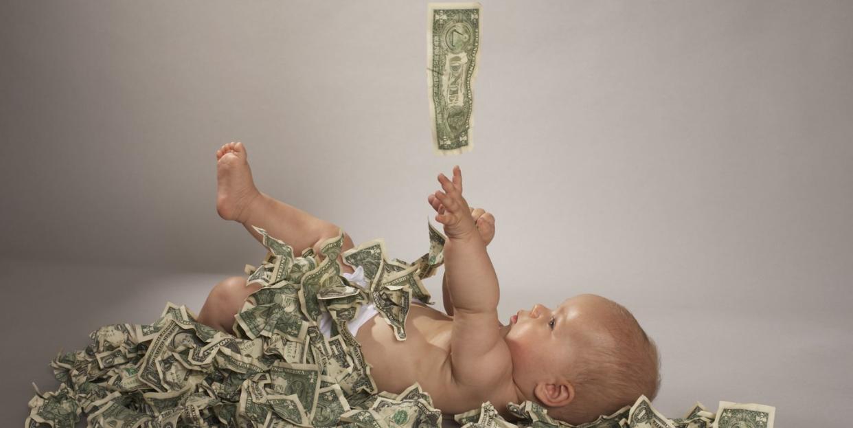 baby girl 5 months lying down covered with us dollar bills falling from above