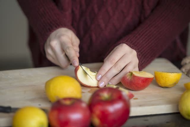 <p>Westend61 / Getty Images</p> Hands of young female cutting fruits on wooden board, close-up