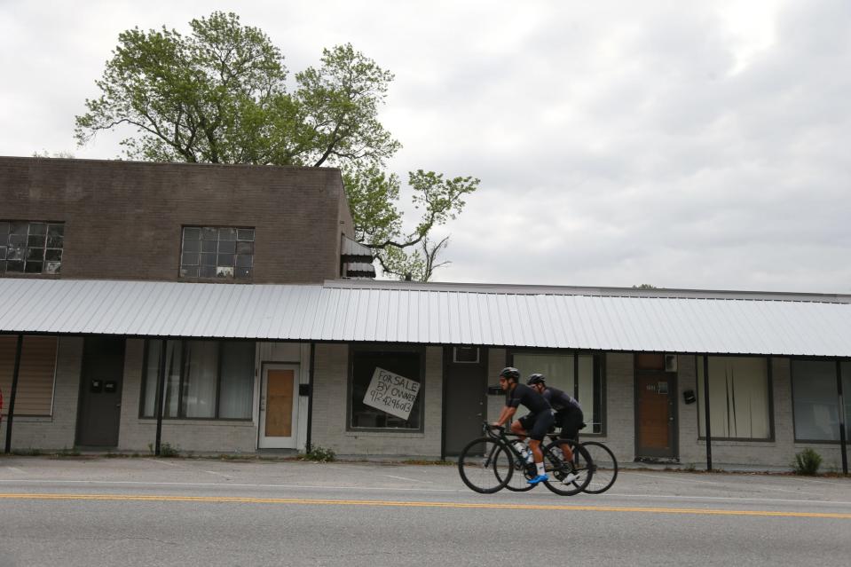 Bicycle riders pass an empty store front along South Coastal Highway in Port Wentworth.