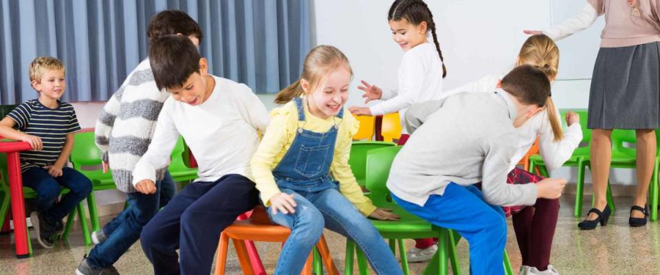 Happy laughing pupils of primary school having fun during break with their teacher, playing musical chairs