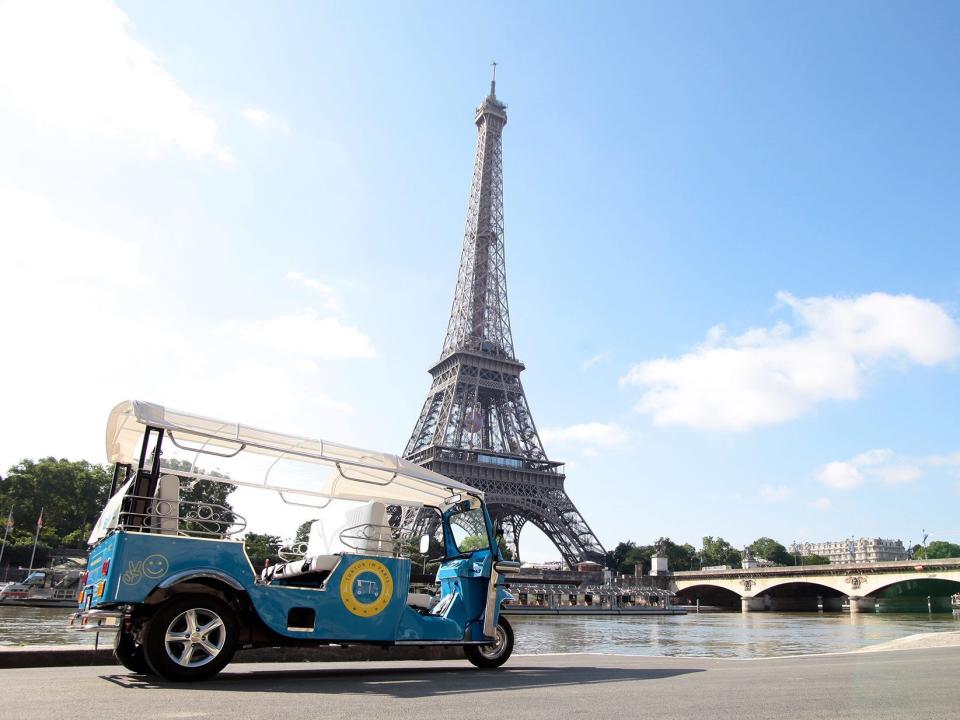 A small, blue vehicle similar to a golf cart is parked in front of the Eiffel Tower