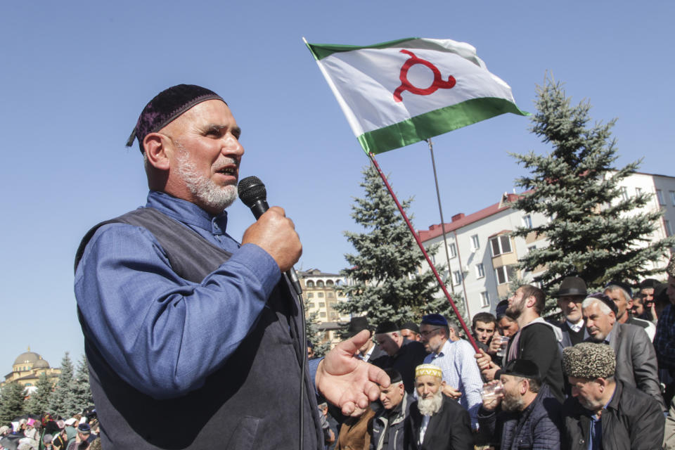 A man talks to the crowd gathered as an Ingushetia flag is displayed, during a protest against the new land swap deal agreed by the heads of the Russian regions of Ingushetia and Chechnya, in Ingushetia's capital Magas, Russia, Monday, Oct. 8, 2018. Ingushetia and the neighboring province of Chechnya last month signed a deal to exchange what they described as unpopulated plots of agricultural land, but the deal triggered massive protests in Ingushetia where it was seen by many as hurting Ingushetia’s interests. (AP Photo/Musa Sadulayev)