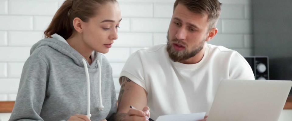 White millennial couple in their kitchen shopping for mortgage rates on their laptop.