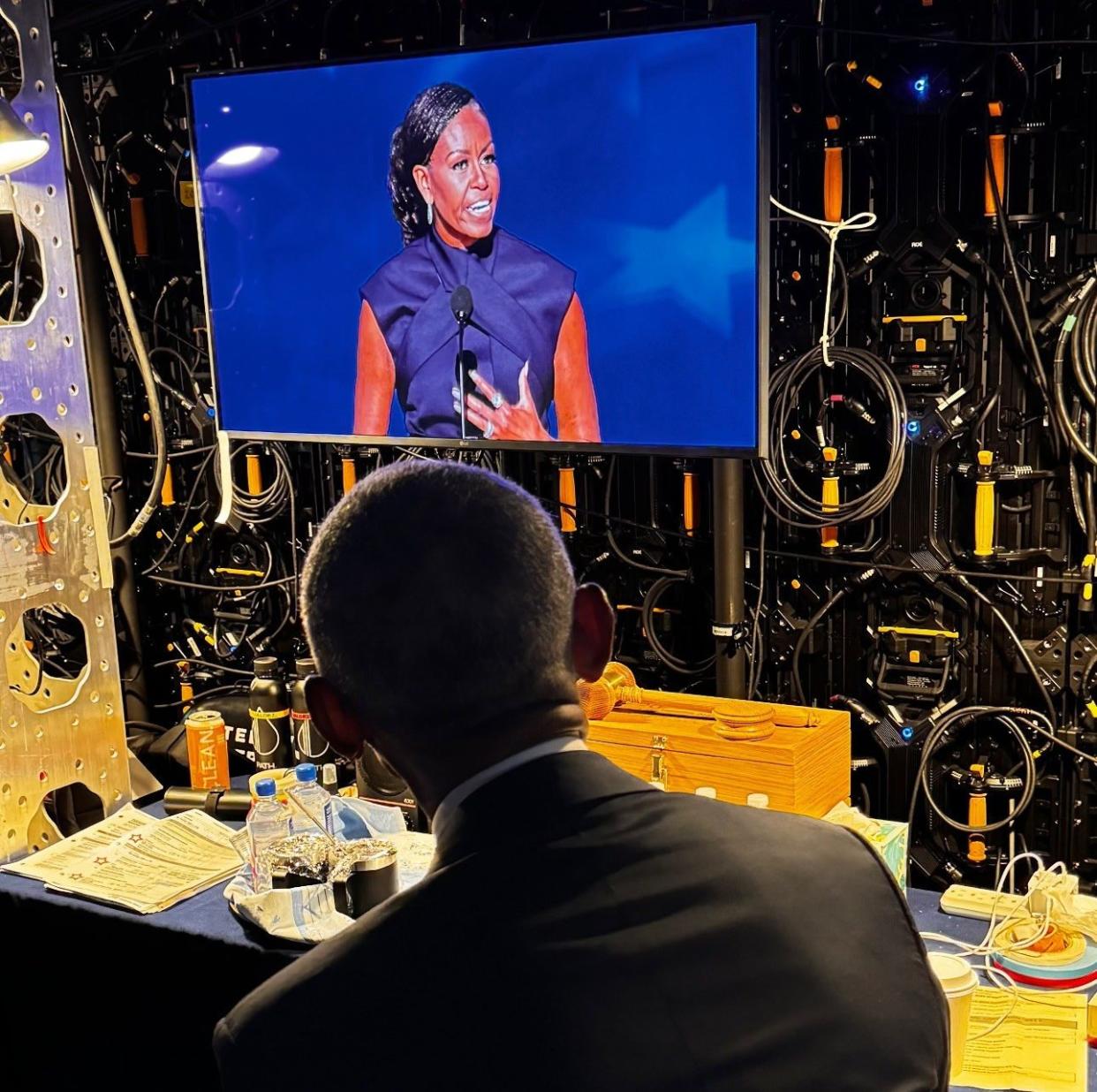 Barack Obama watches his wife Michelle Obama on screen at the DNC