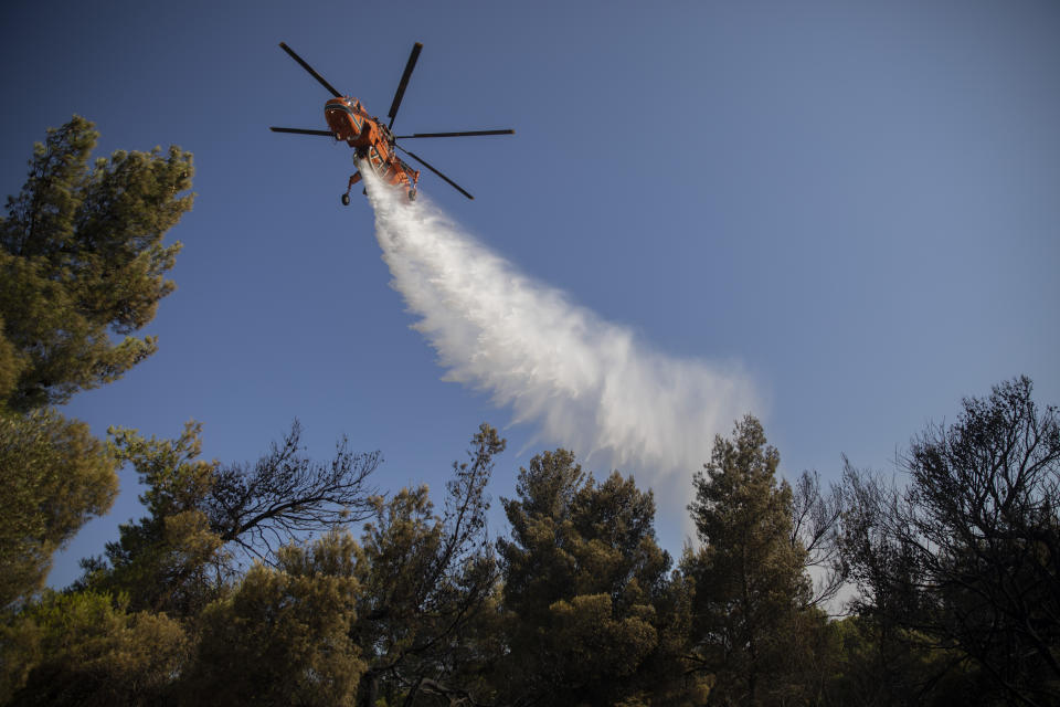 A firefighting helicopter drops water onto a wildfire in the town of Rafina, near Athens, on Tuesday, July 23, 2019. A forest fire outside Athens is threatening homes on the anniversary of a deadly blaze in the same area that claimed more than 100 lives. (AP Photo/Petros Giannakouris)