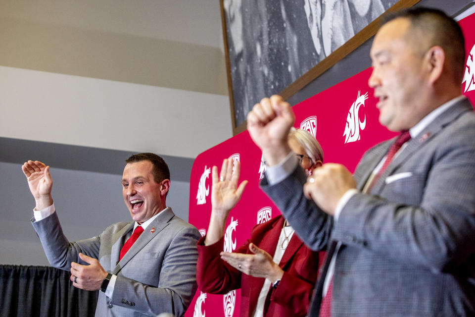 New Washington State football coach Jake Dickert, left, reacts during the playing of the school's fight song at a news conference Thursday, Dec. 2, 2021, in Pullman, Wash. Dickert, 38, was elevated last week from interim coach after the team pounded rival Washington in the annual Apple Cup game in Seattle. (August Frank/Lewiston Tribune via AP)