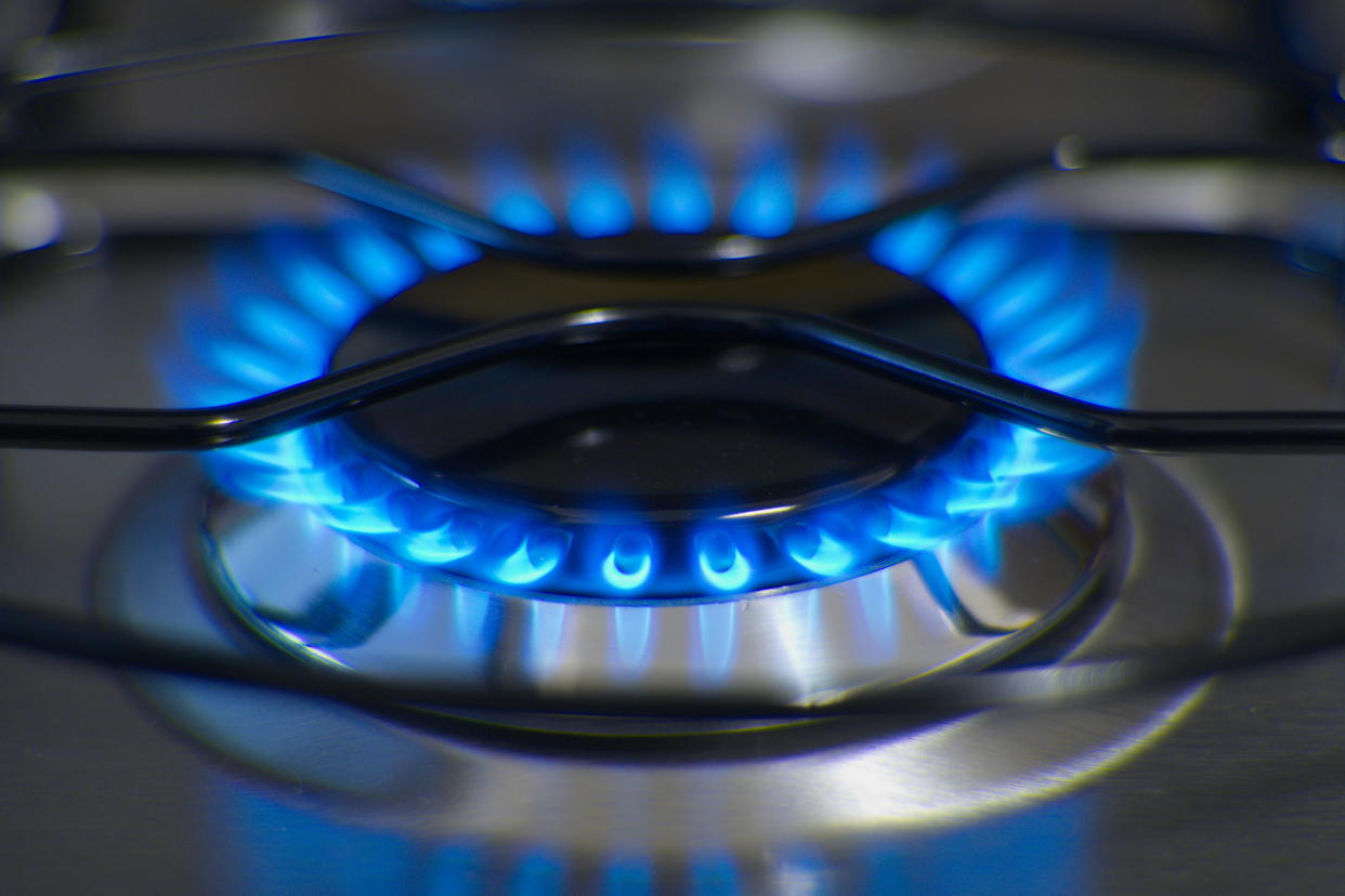 Flames of a gas burner and an iron trivet on a stainless steel stove.