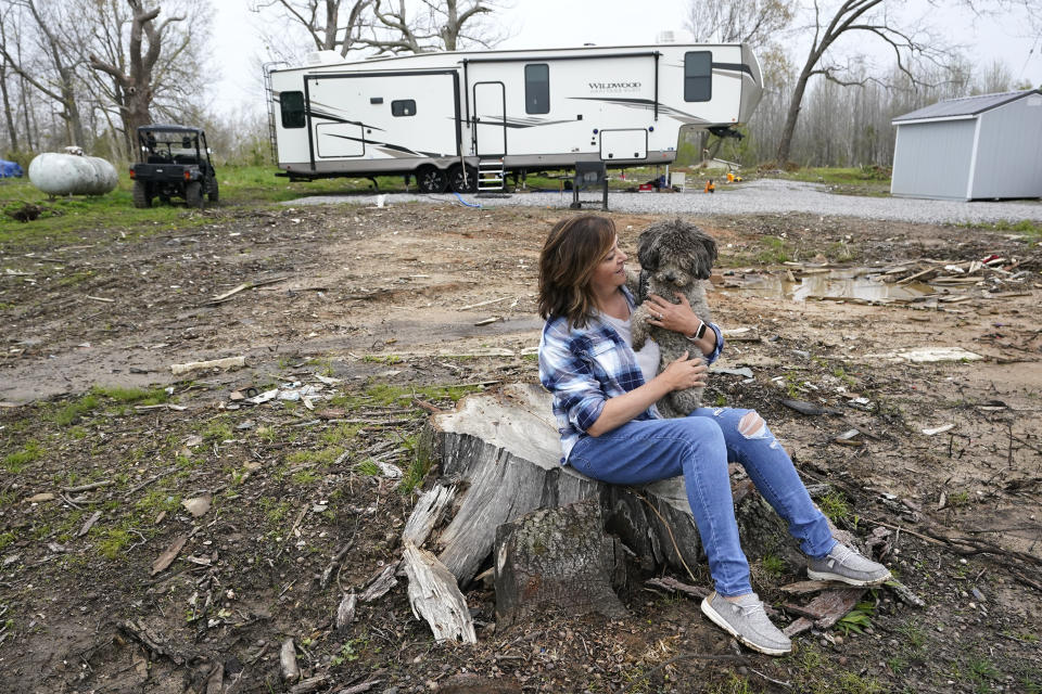 FILE -Chris Bullock holds her dog, Dewey, April 21, 2022, as she sits on the stump of the tree that fell on her son's home, which originally stood behind her, in Dawson Springs, Ky. Chris Bullock has a lot to be grateful for as she decorates her new home for Christmas, after spending much of the past year in a camper with her family. One year ago Saturday, Dec. 10, 2022, a massive tornado obliterated wide swaths of her Kentucky hometown of Dawson Springs, leaving her homelessaftera terrifying night of death and destruction.(AP Photo/Mark Humphrey, File)