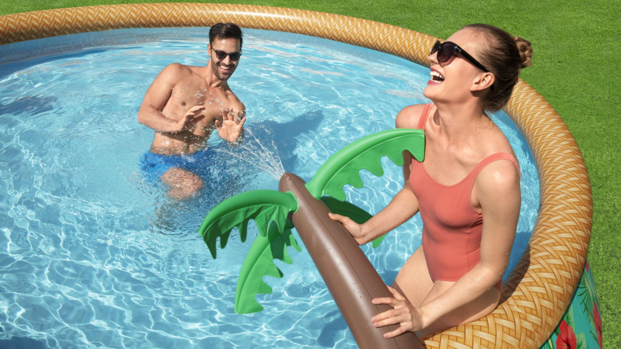  Image of a woman spraying a man with a palm tree sprinkler in an inflatable swimming pool 