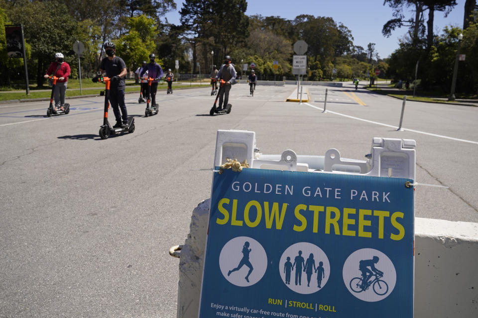 A group of people on electric scooters ride along car-free John F. Kennedy Drive in Golden Gate Park, Wednesday, April 28, 2021, in San Francisco. At the start of the pandemic, San Francisco closed off parts of a major beachfront highway and Golden Gate Park to cars so that people had a safe place to run and ride bikes. Open space advocates want to keep those areas car-free as part of a bold reimagining of how U.S. cities look. But opponents decry the continued closures as elitist, unsafe and nonsensical now that the pandemic is over and people need to drive again. (AP Photo/Eric Risberg)