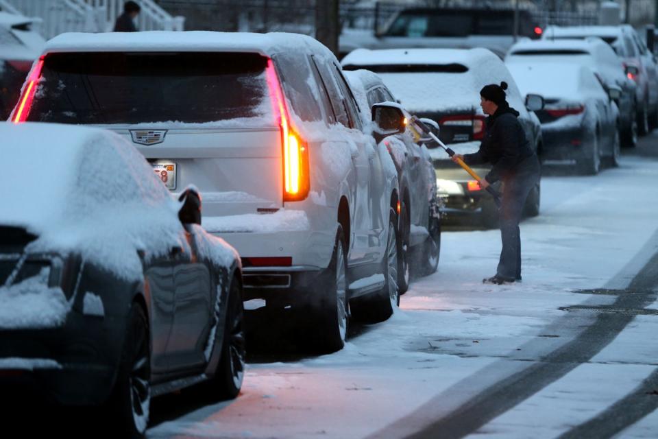 <p>Jonathan Wiggs/The Boston Globe via Getty</p> A woman clears snow from her car