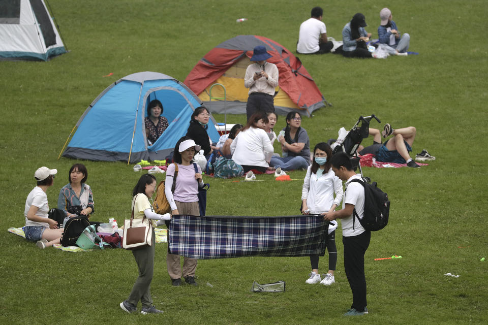 A woman wearing a face mask to help curb the spread of the coronavirus as her friends prepare to set up a picnic cloth on a scenic mountain in Yanqing, outskirt of Beijing on Sunday, Aug. 30, 2020. China currently has more than 200 people being treated in hospital for COVID-19, with another over 300 in isolation after testing positive for the virus without displaying symptoms.(AP Photo/Andy Wong)