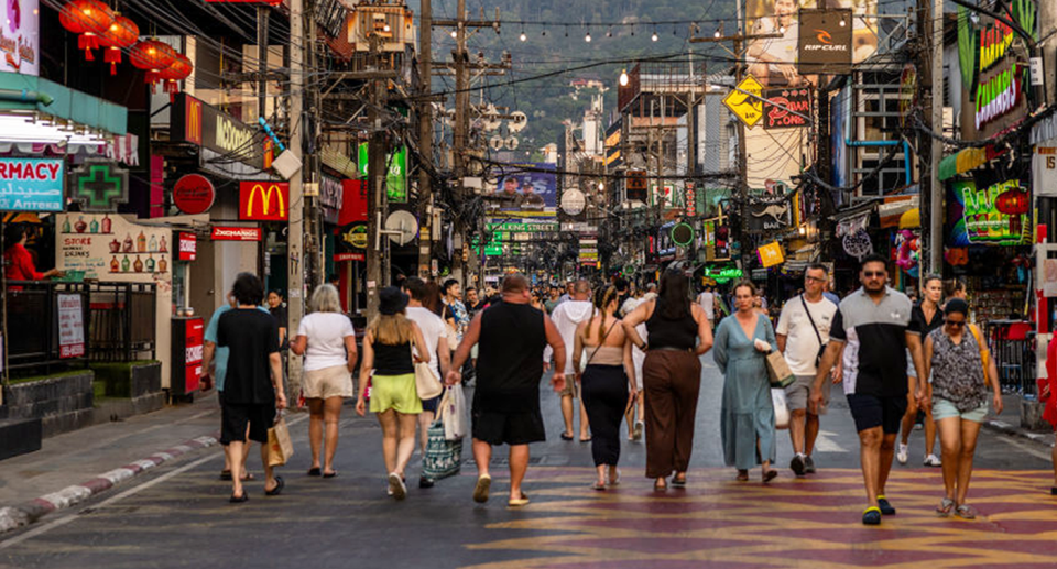 游客沿着泰国一条繁忙的街道行走，背景是一家大麻店。