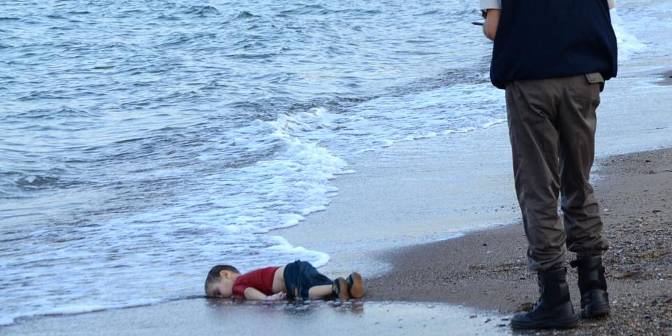 A Turkish police officer stands next to a migrant child’s body off the shores in Bodrum, southern Turkey, on September 2, 2015 after a boat carrying refugees sank while reaching the Greek island of Kos. The child’s name was Alan Kurni (born Aylan Shenu). Photo: NILUFER DEMIR/AFP via Getty Images