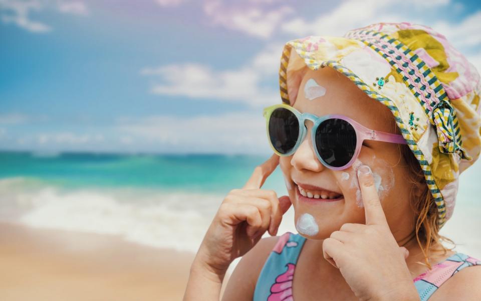 child applying sunscreen to face on beach