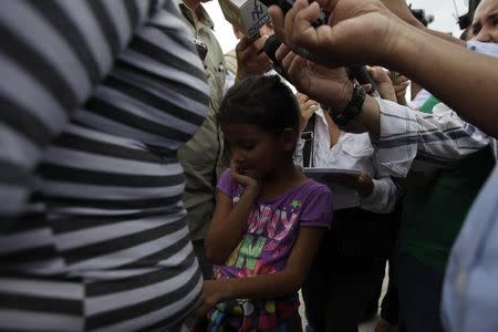 A girl gestures while her mother is interviewed by reporters after being deported from the U.S. at the international airport in San Pedro Sula, northern Honduras July 14, 2014. REUTERS/Jorge Cabrera