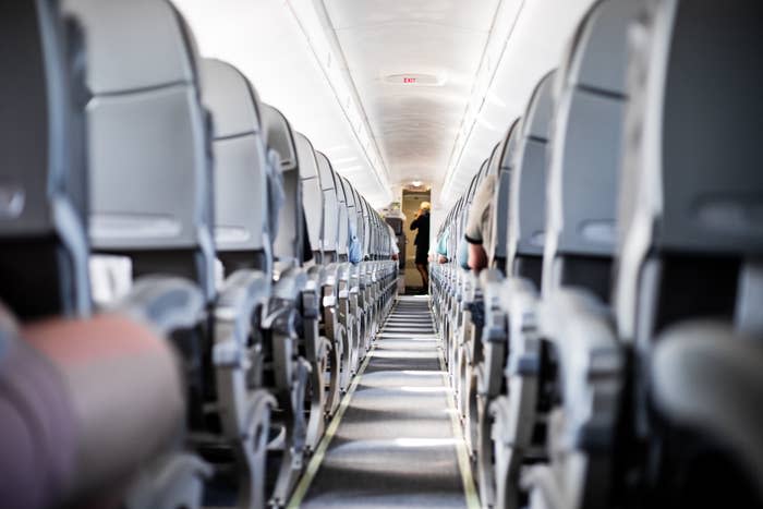 Empty airplane aisle with rows of vacant seats, with a single person standing near the exit at the back of the plane