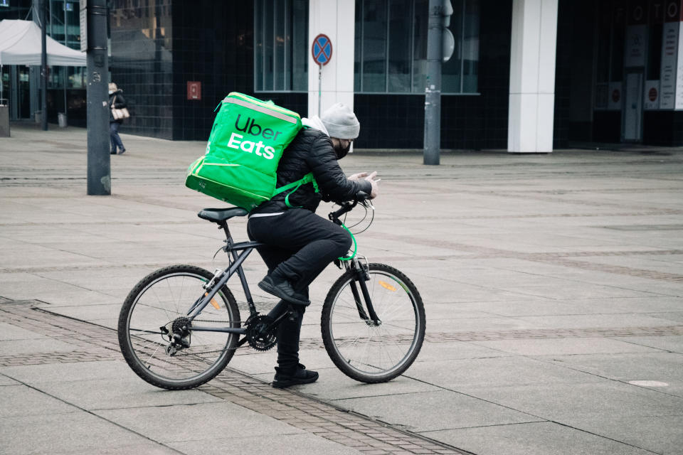 KATOWICE. POLAND - March 26, 2021: Driver man on bike or motorcycle for fast restaurant deliver. Food courier bag for delivery takeaway service. Uber eats courier on scooter delivering food