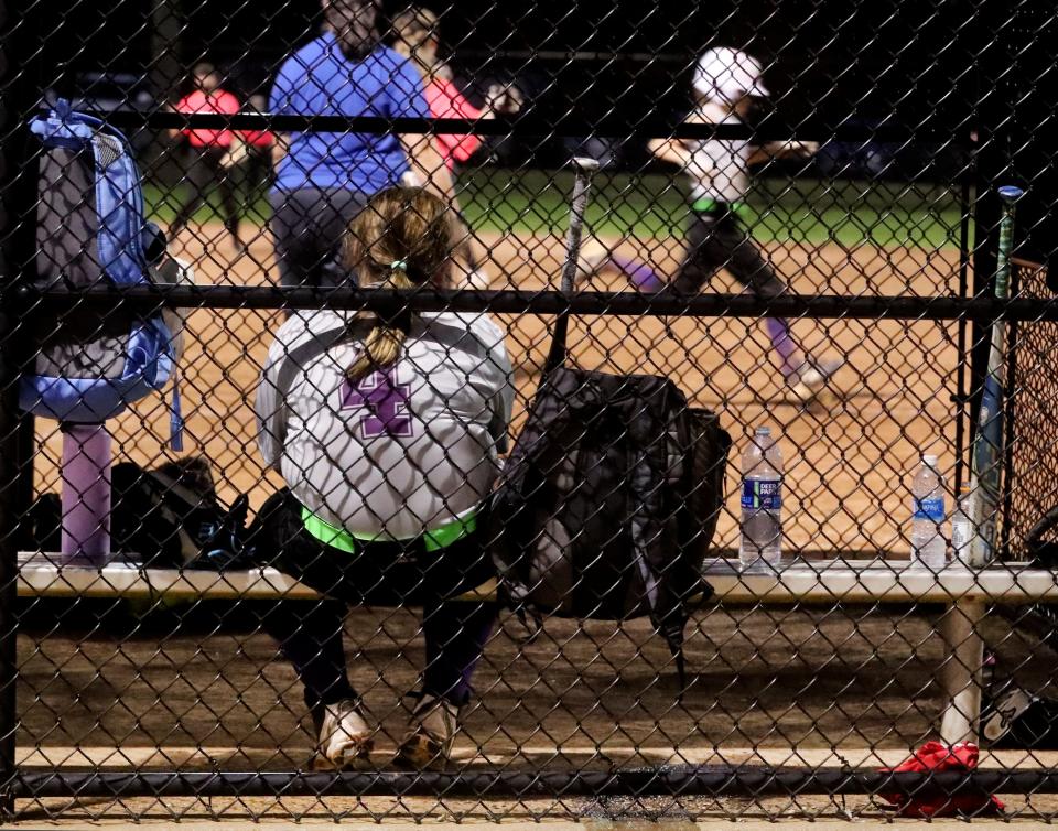 A softball player sits in the dugout waiting to bat while her teammate runs to first plate in the background during a softball game at McKnight Park on Tuesday, Sept. 5, 2023.