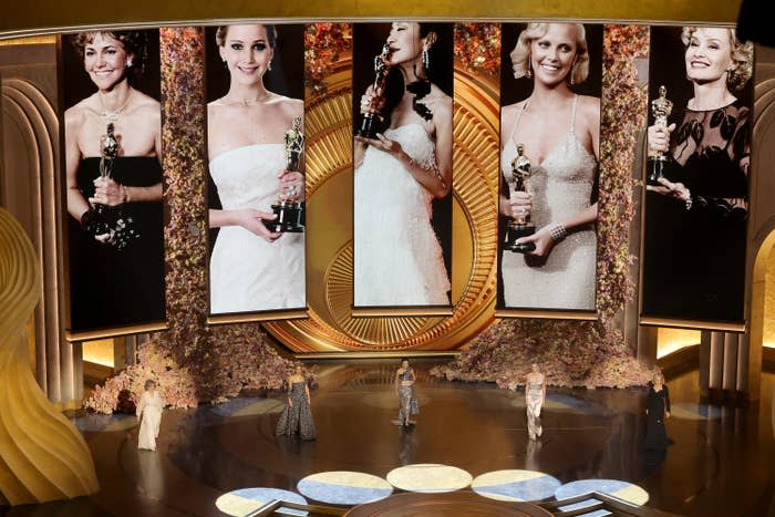 Award show stage with large screens displaying past female Oscar winners holding trophies