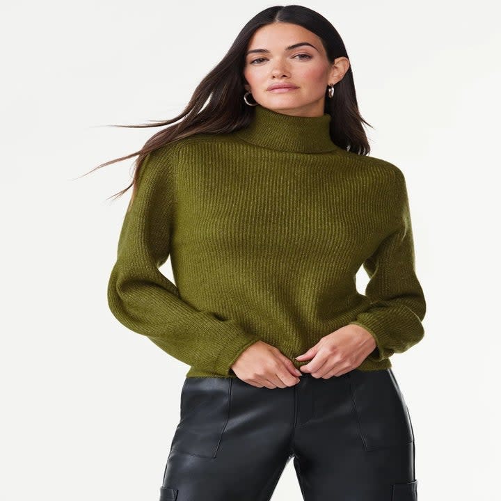 A model wearing the sweater in green with black leather pants
