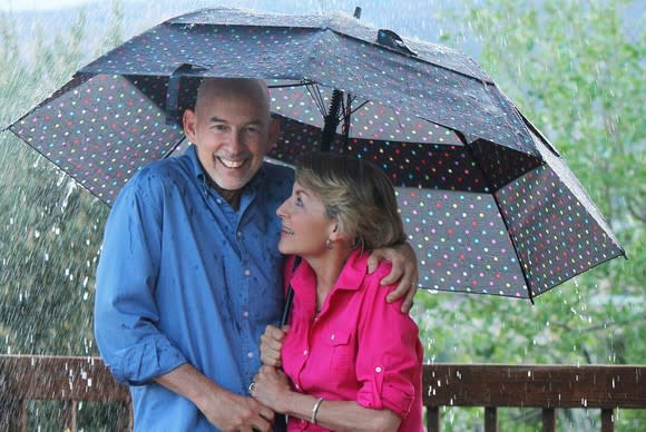 Older couple smile as they stand huddled under an umbrella in the rain