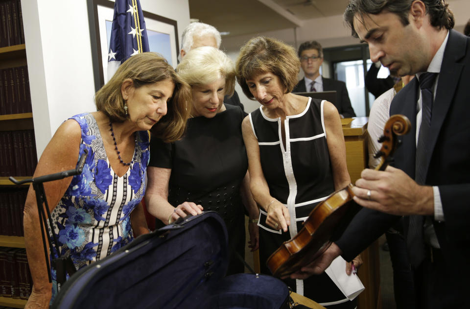 FILE - In an August 6, 2015 file photo, FBI agent Chris McKeogh, right, shows sisters Amy Totenberg, left, Nina Totenberg, second from left, and Jill Totenberg the Ames Stradivarius violin that was stolen from their father 35 year ago, in New York. The Stradivarius violin stolen four decades ago from the late virtuoso Roman Totenberg and returned to his family by a federal prosecutor came alive again _ at the crime scene, playing the same music. At a concert in Cambridge, Massachusetts, 19-year-old star violinist Nathan Meltzer revived the priceless instrument of the Polish-born musician on Friday evening, Nov. 15, 2019. (AP Photo/Seth Wenig, File)