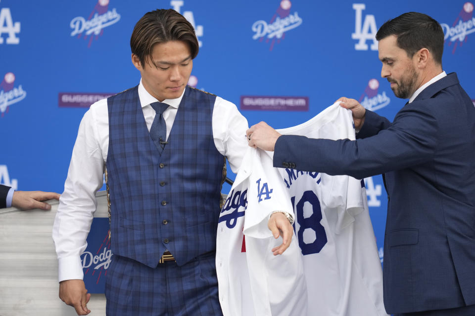 Yoshinobu Yamamoto, left, puts on a Dodgers jersey with help form Executive Vice President and General Manager Brandon Gomes during his introduction as a new member of the Los Angeles Dodgers baseball team Wednesday, Dec. 27, 2023, in Los Angeles. (AP Photo/Ashley Landis)