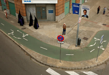 FILE PHOTO: Penitents of San Bernardo brotherhood walk in front of an electoral poster of Spain's People's Party (PP) leader and presidential candidate Pablo Casado in the Andalusian capital of Seville, Spain April 17, 2019. REUTERS/Marcelo del Pozo