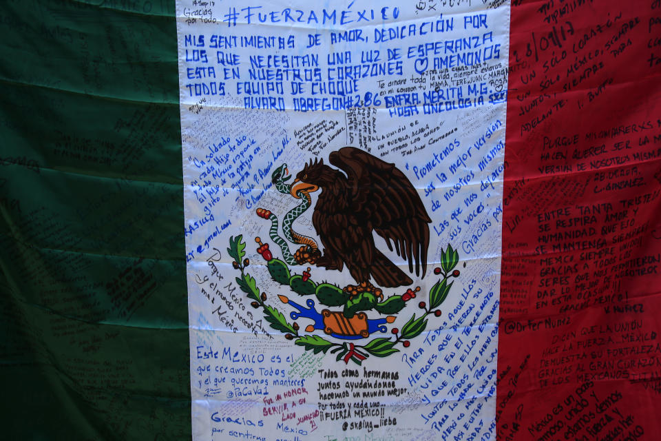 A Mexican flag printed with messages hangs on the wall during a memorial ceremony in front of the site at Alvaro Obregon 286 where 49 died when their office building collapsed in last year's 7.1 magnitude earthquake, in Mexico City, Wednesday, Sept. 19, 2018. Across the city, memorials were held at sites where hundreds perished in the Sept. 19, 2017 quake.(AP Photo/Rebecca Blackwell)