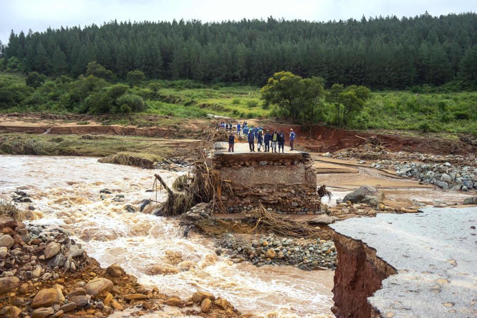 Timber company workers stand stranded on a damaged road on March 18, 2019, in eastern Zimbabwe after the area was hit by Cyclone Idai. Idai tore through the centre of Mozambique on March 14 before barreling into neighboring Zimbabwe, bringing flash floods and ferocious winds and washing away roads and houses. Over 1,000 people are feared dead.