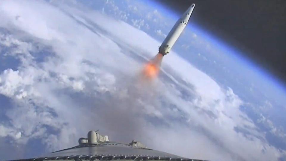 a large white rocket rises through a cloudy sky above a huge plume of fire and smoke