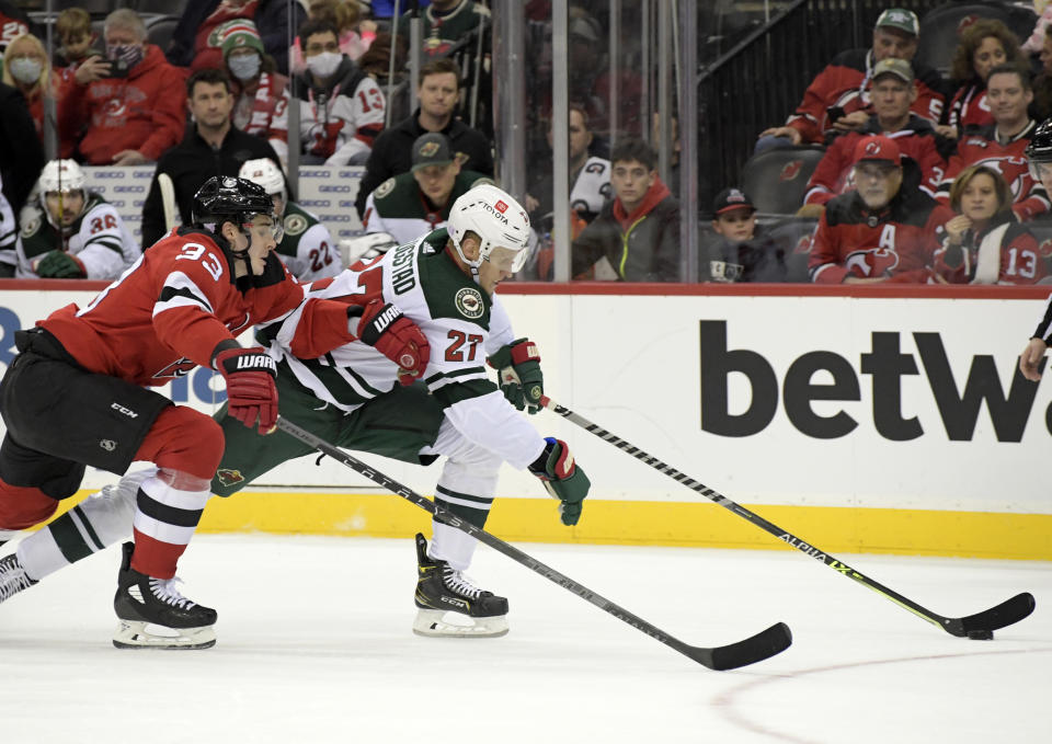 Minnesota Wild center Nick Bjugstad (27) skates with the puck as he is pursued by New Jersey Devils defenseman Ryan Graves (33) during the second period of an NHL hockey game Wednesday, Nov.24, 2021, in Newark, N.J. (AP Photo/Bill Kostroun)