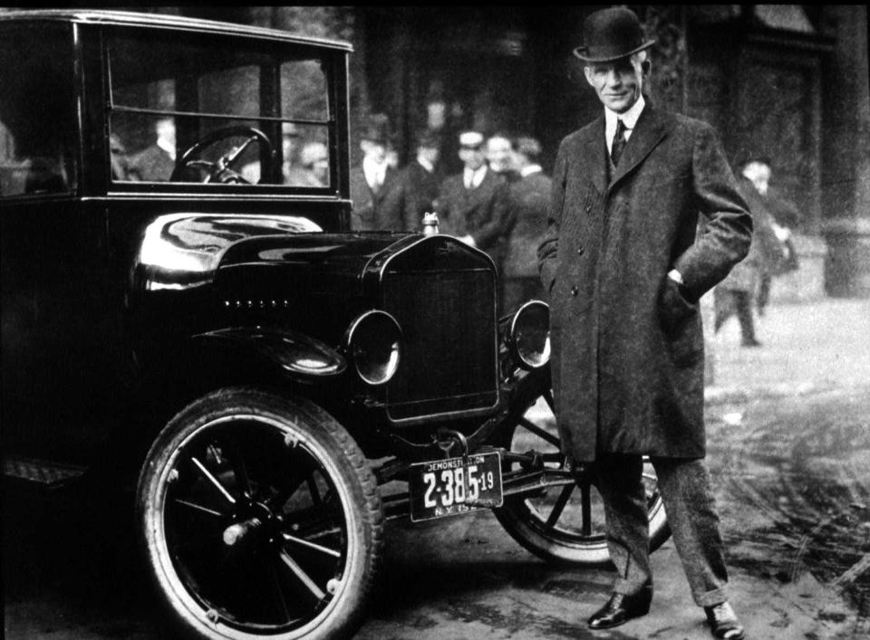 Henry Ford standing next to a Ford automobile.