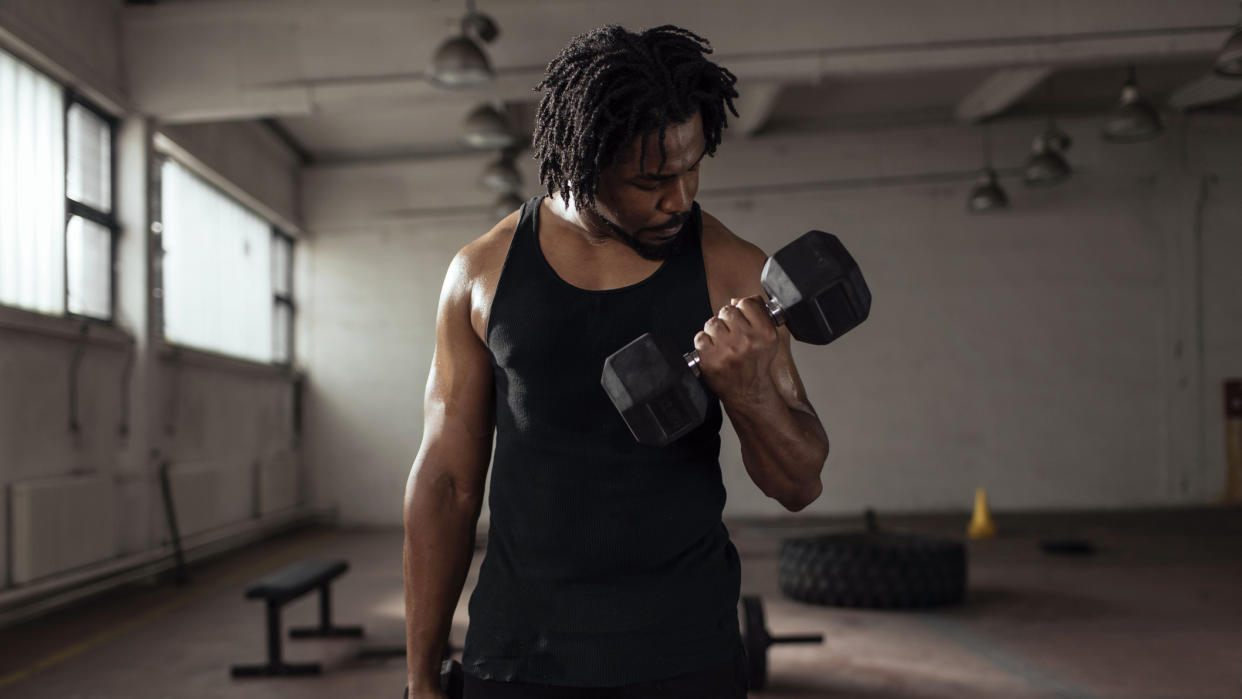  Man doing bicep curl with dumbbell in a gym. 