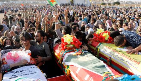 Mourners gesture "V" sign next to the coffins of two Kurdish fighters and a Syrian journalist killed by the Islamic State militants at the frontline in Deir al-Zour, during a funeral at the cemetery in Kobani, Syria October 14, 2017. REUTERS/Erik De Castro