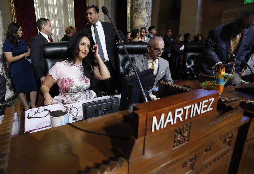 Nury Martinez, in a pink dress, is shown sitting in the City Council chambers before a wooden plaque that bears her name